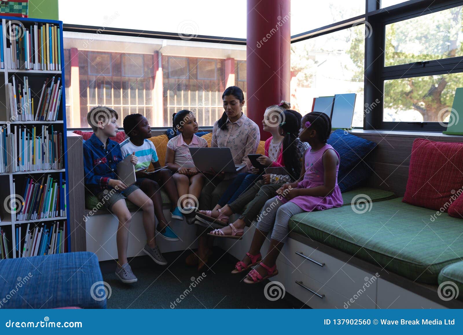 Female Teacher Studying Student on Laptop while Sitting on the Couch in School Library Stock