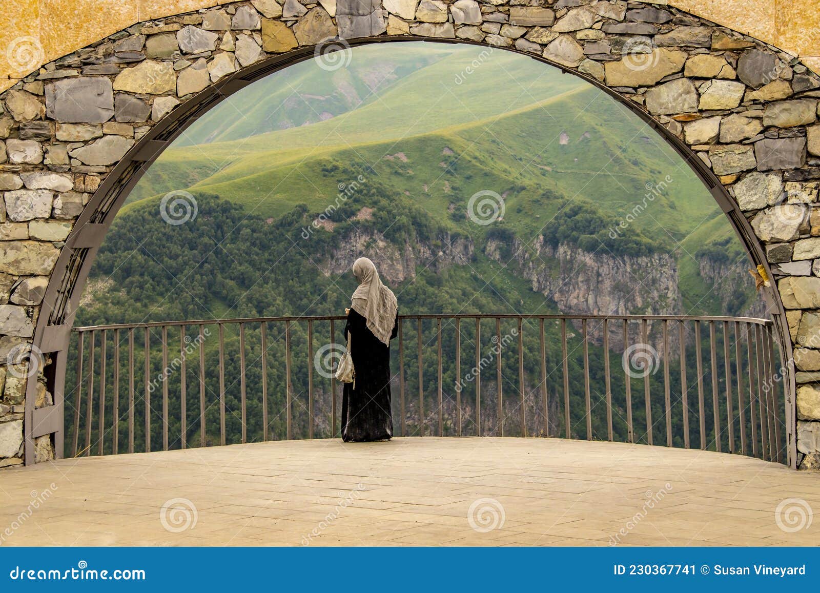 female tourist in abaya and hijÃÂb checks phone standing in arch of georgia friendship monument on military highway with beautiful