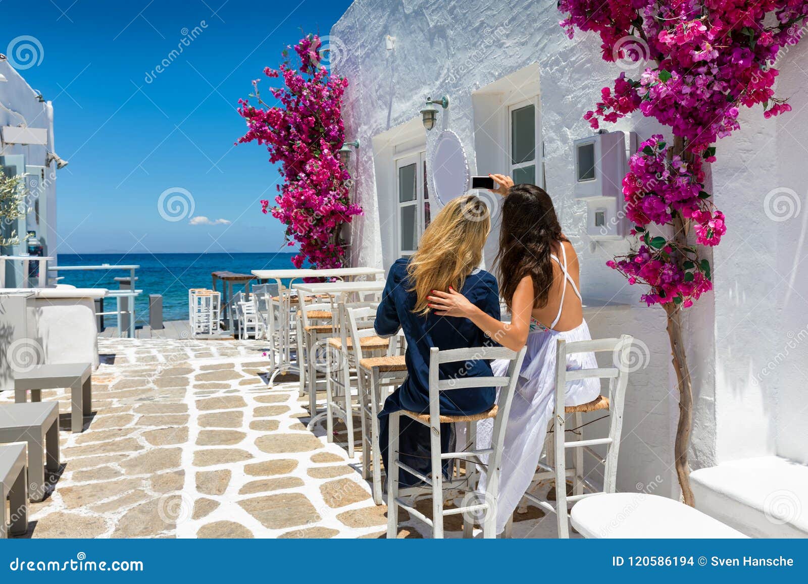 female tourists are taking a selfie photo in the whitewashed alleys of naousa village on paros