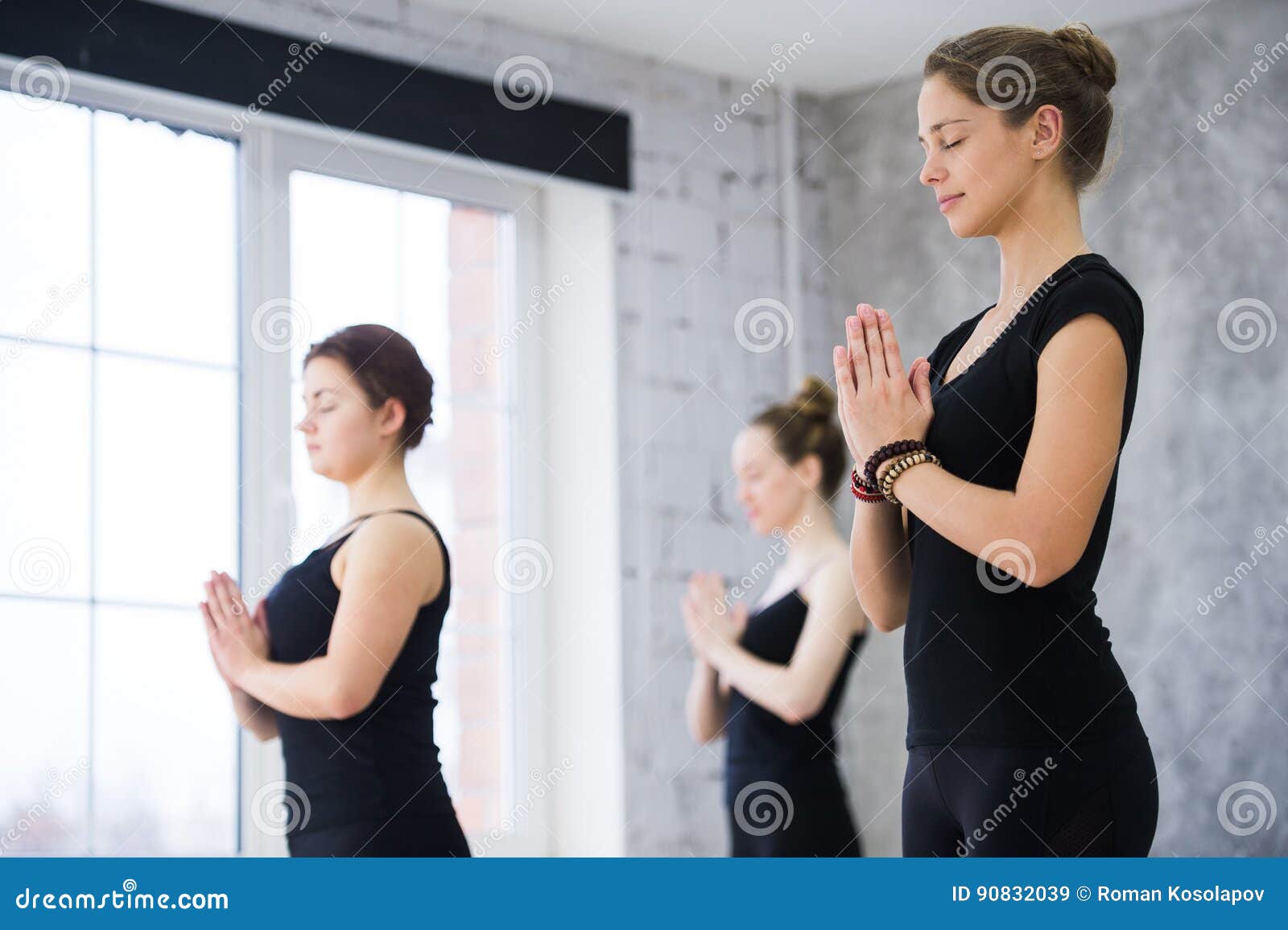 Female Trainer with Class Standing in Namaste Pose at Yoga Class Stock