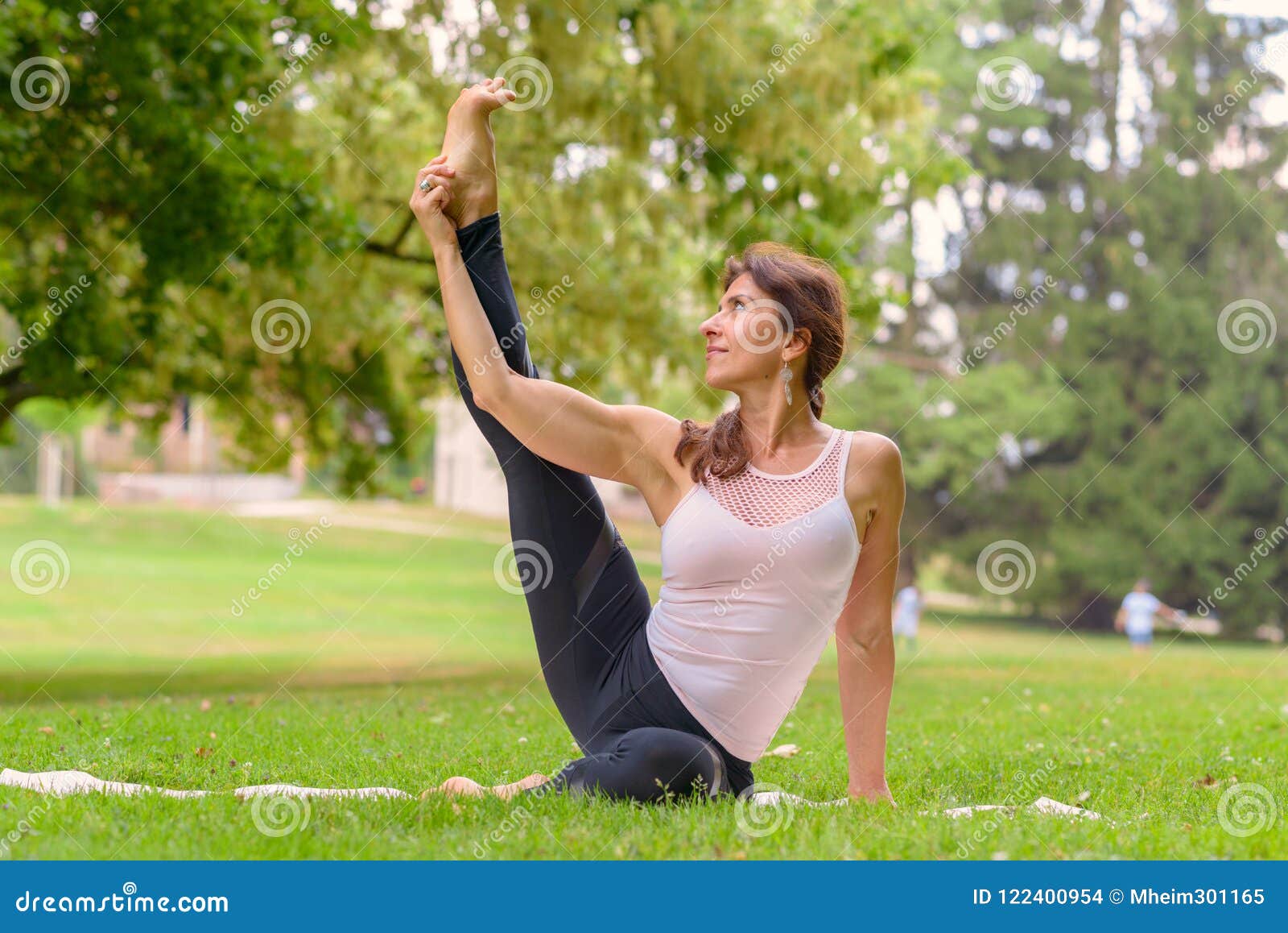 Female Yoga Artist Doing Leg Exercises In Meadow Stock