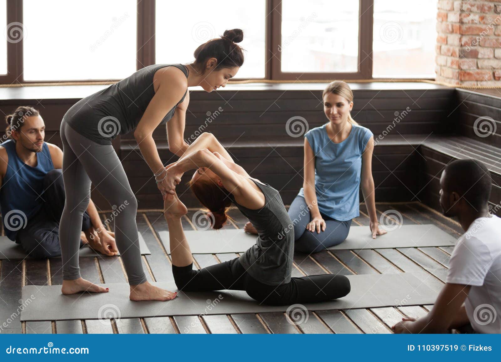 Female Yoga Instructor Helping Woman Doing Exercise at Group Tra Stock