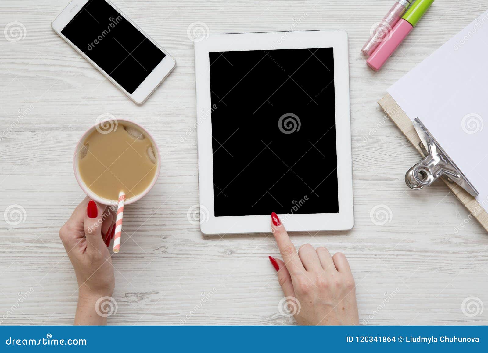 feminine work space with tablet, noticepad, sheet, latte ice, smartphone and female hands over white wooden background, top view.