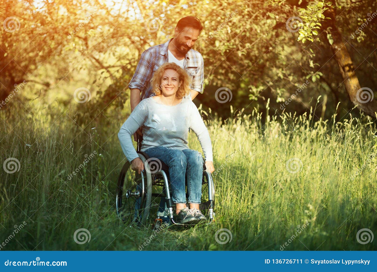 Femme De Sourire Dans Le Fauteuil Roulant Avec Le Mari En Parc Le Jour Ensoleillé Image Stock