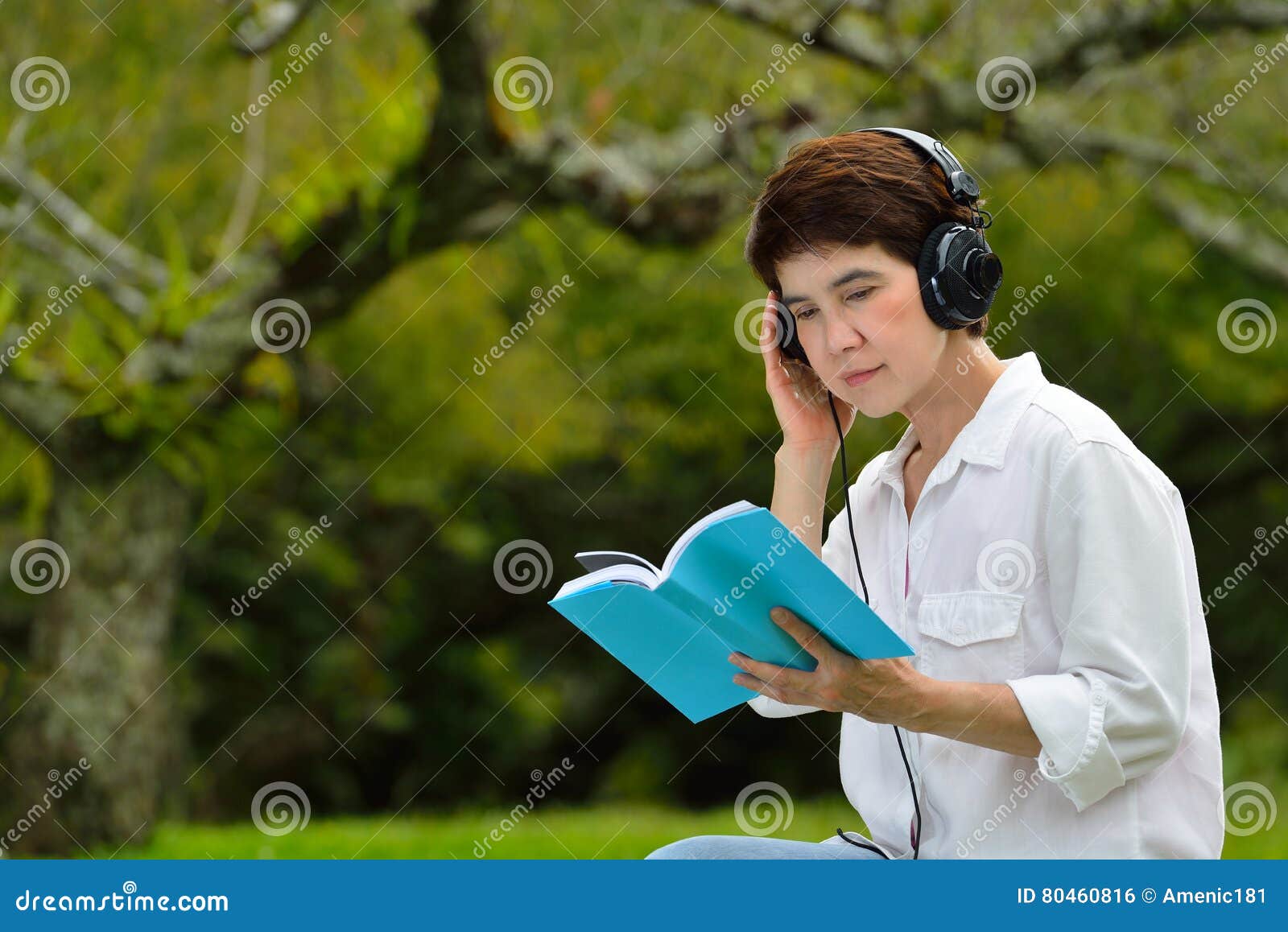Le milieu a vieilli la femme lisant un livre et appréciant la musique avec des écouteurs en parc
