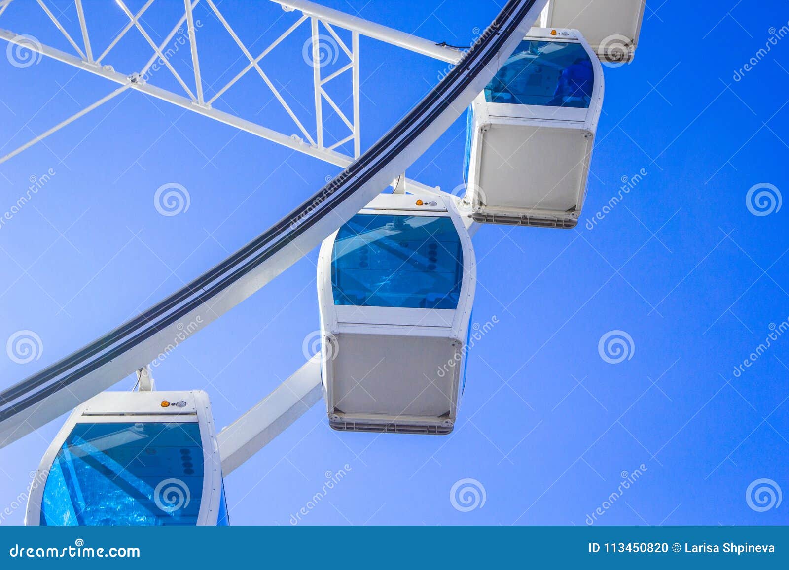 White Ferris Wheel With Glass Light Blue Cabins Against A Blue Sky