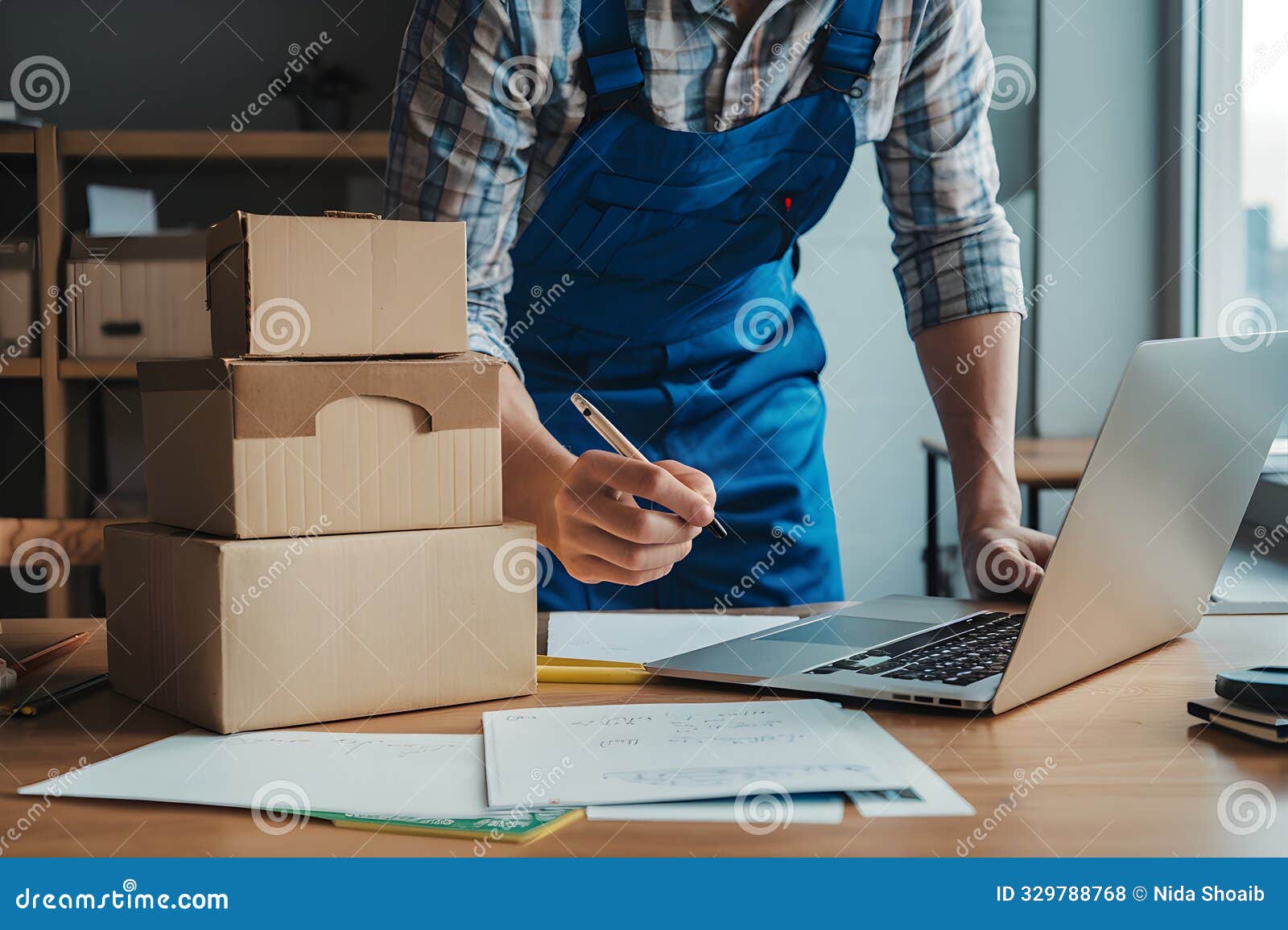 figure in blue overalls writes on stacked boxes beside window and laptop
