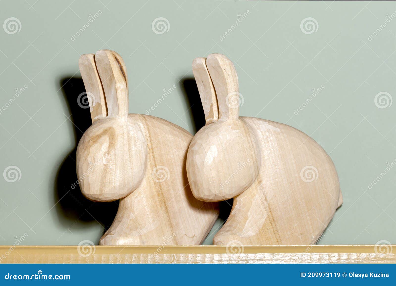 two figurines of wooden hares on a shelf against a background of a green wall