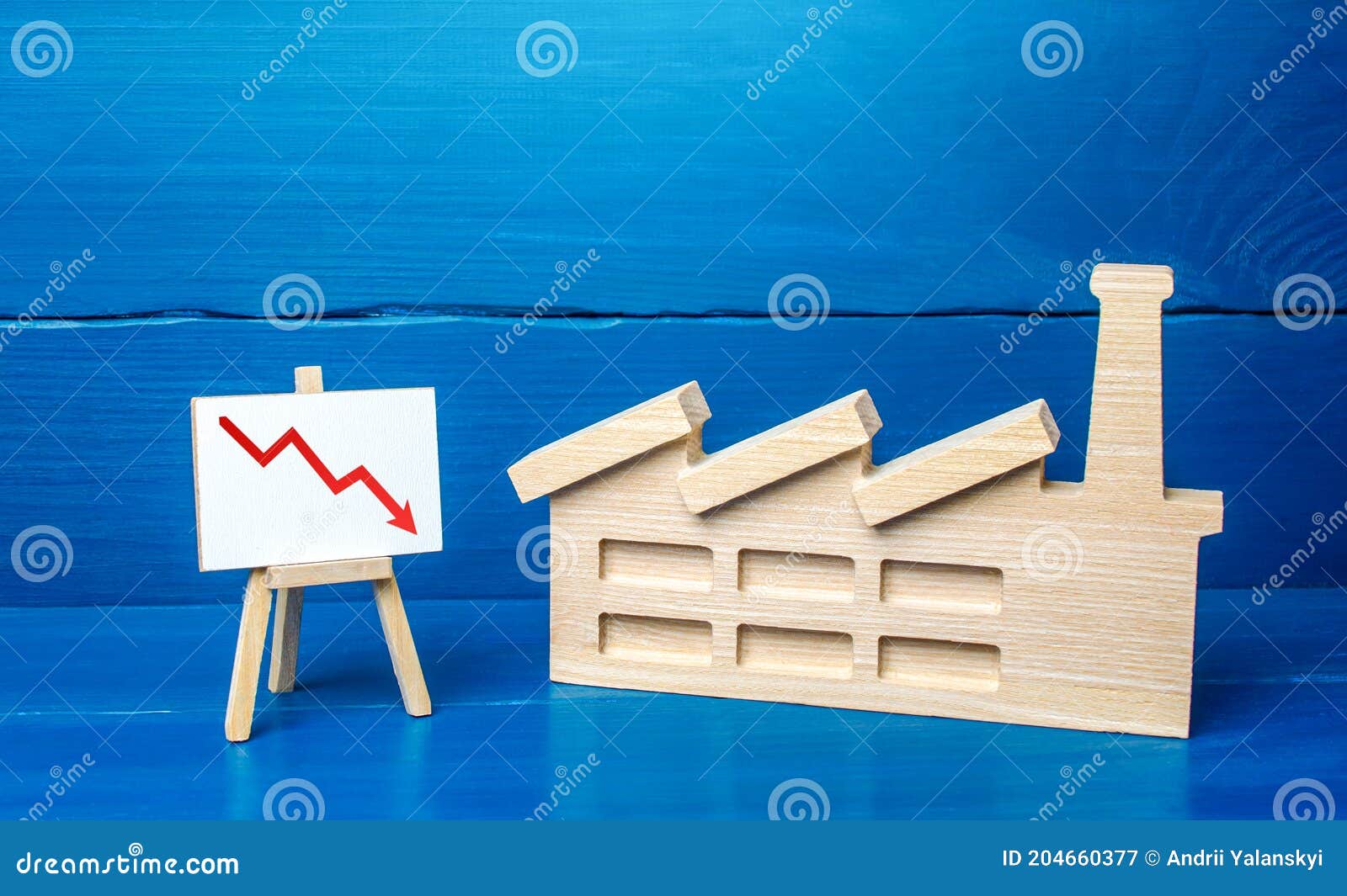figurine of industrial factory plant and easel with a red down arrow chart. decreased production volumes, low income, energy