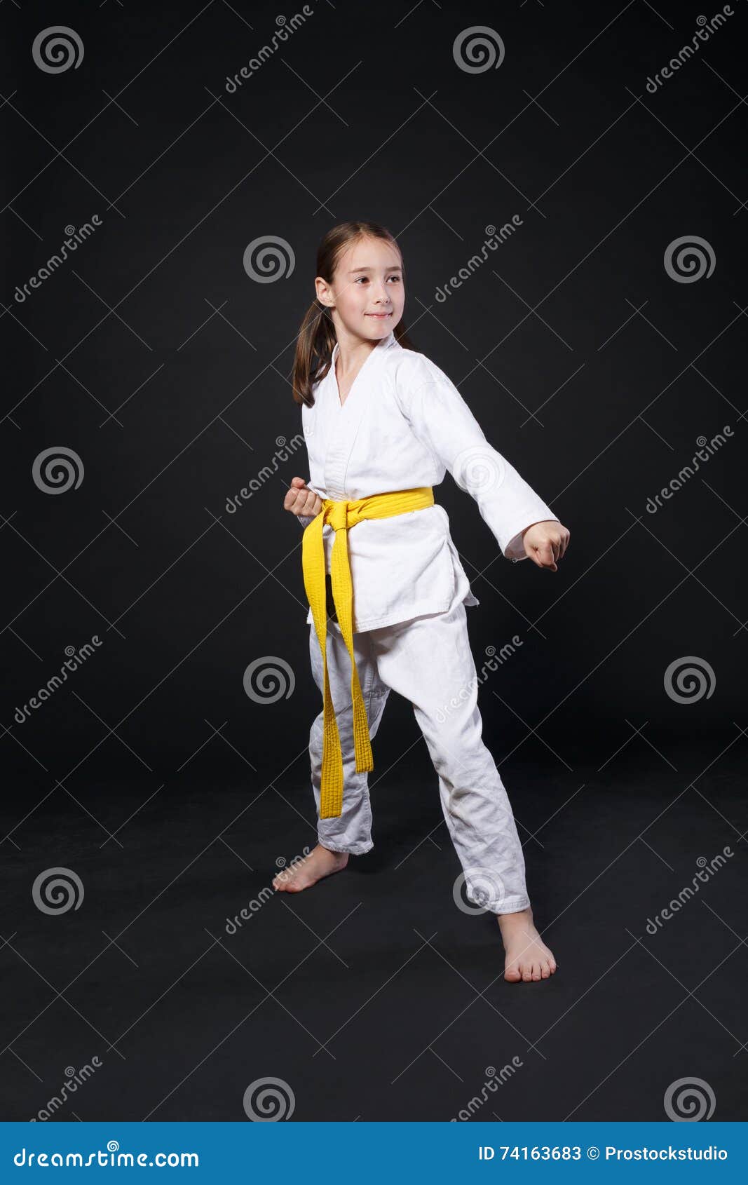 Petite Fille Dans Le Karaté Costume Kimono En Studio À Fond Noir. Enfant  Femme Montre Judo Ou Karaté Stans En Uniforme Blanc Avec Ceinture Jaune.  Art Martial Sport Individuel Pour Les Enfants.