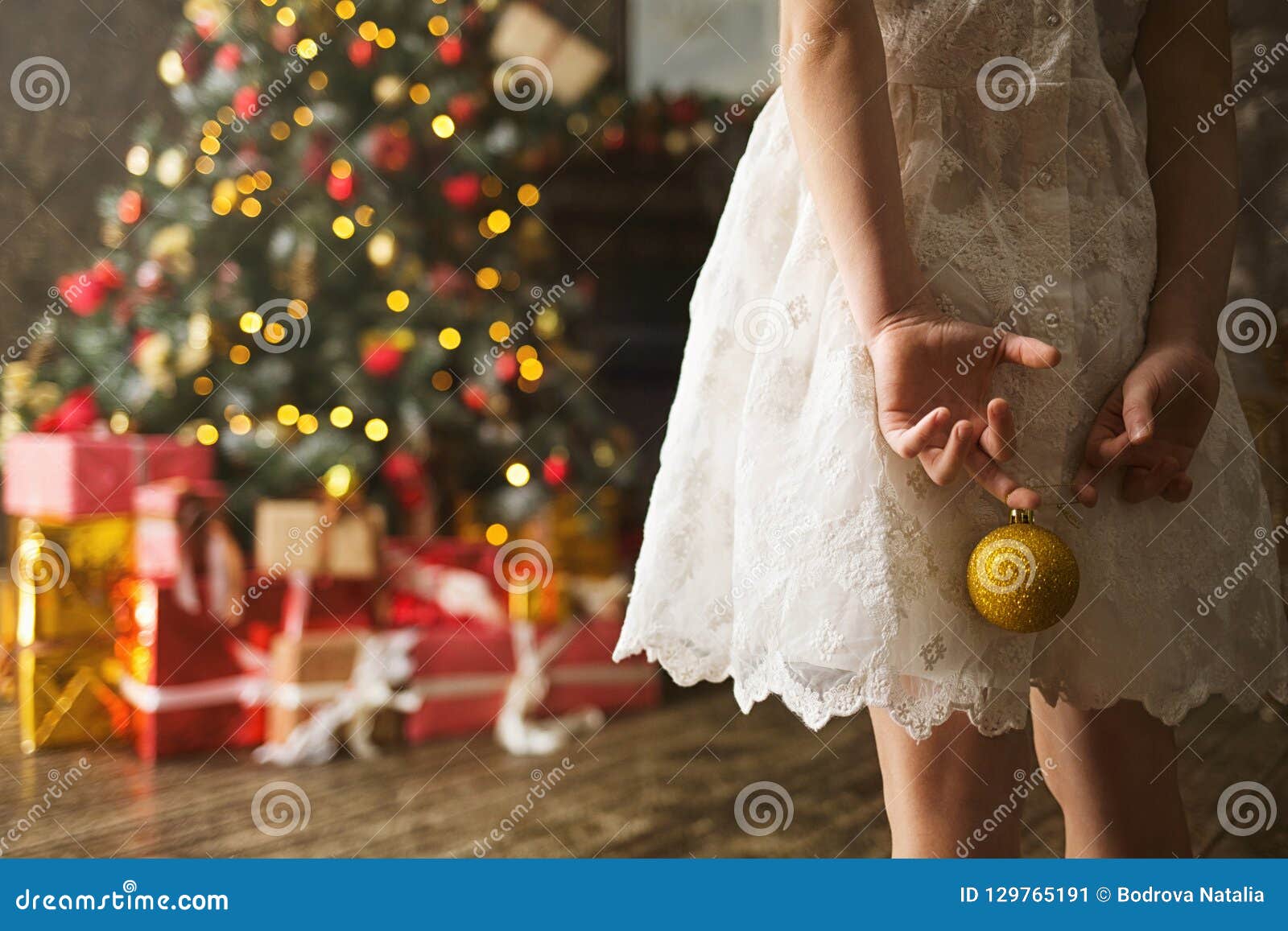 Fille D'enfant Dans Une Robe Blanche Avec Une Boule De Noël Dans Des Ses  Mains Faisant Face à L'arbre De Noël Décoré Avec Beaucou Image stock -  Image du fille, décoration: 129765191