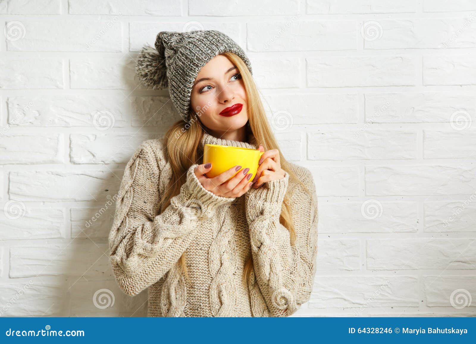 Fille rêvante romantique de hippie d'hiver avec une tasse. Fille rêvante romantique de hippie d'hiver dans le chandail et le Beanie Hat tricotés avec une tasse dans des mains au fond blanc de mur de briques Réchauffage du concept