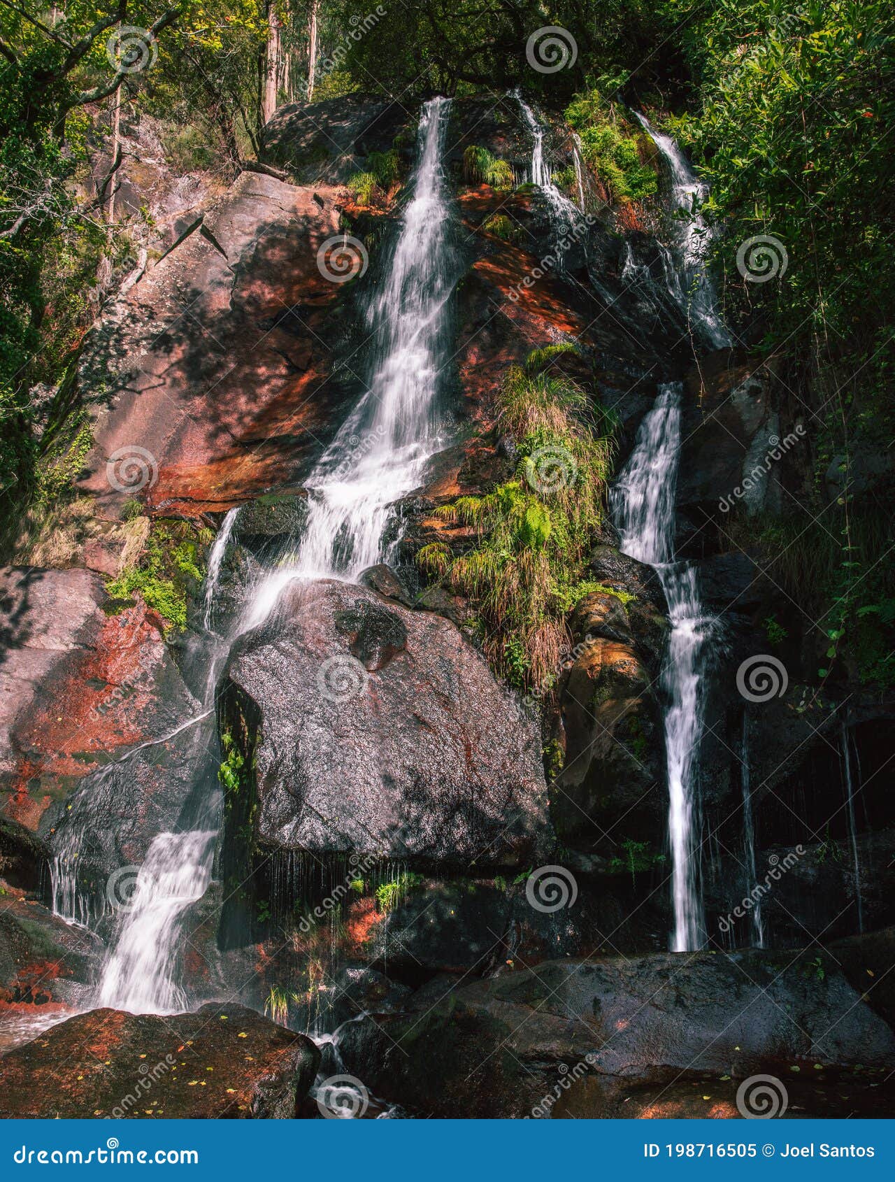 filveda waterfall through green vegetation and red stones