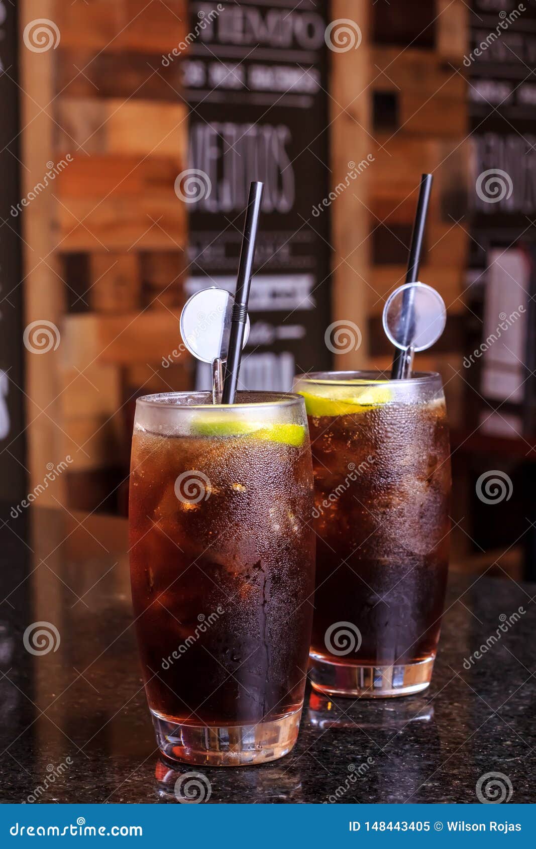 Fin d'angle faible de gourmet moderne glac?. Low angle close up of ice cold modern gourmet craft cocktail of gin and tonic soda garnished by lemon slice and rosemary sprig sprinkled bar background - Imagen