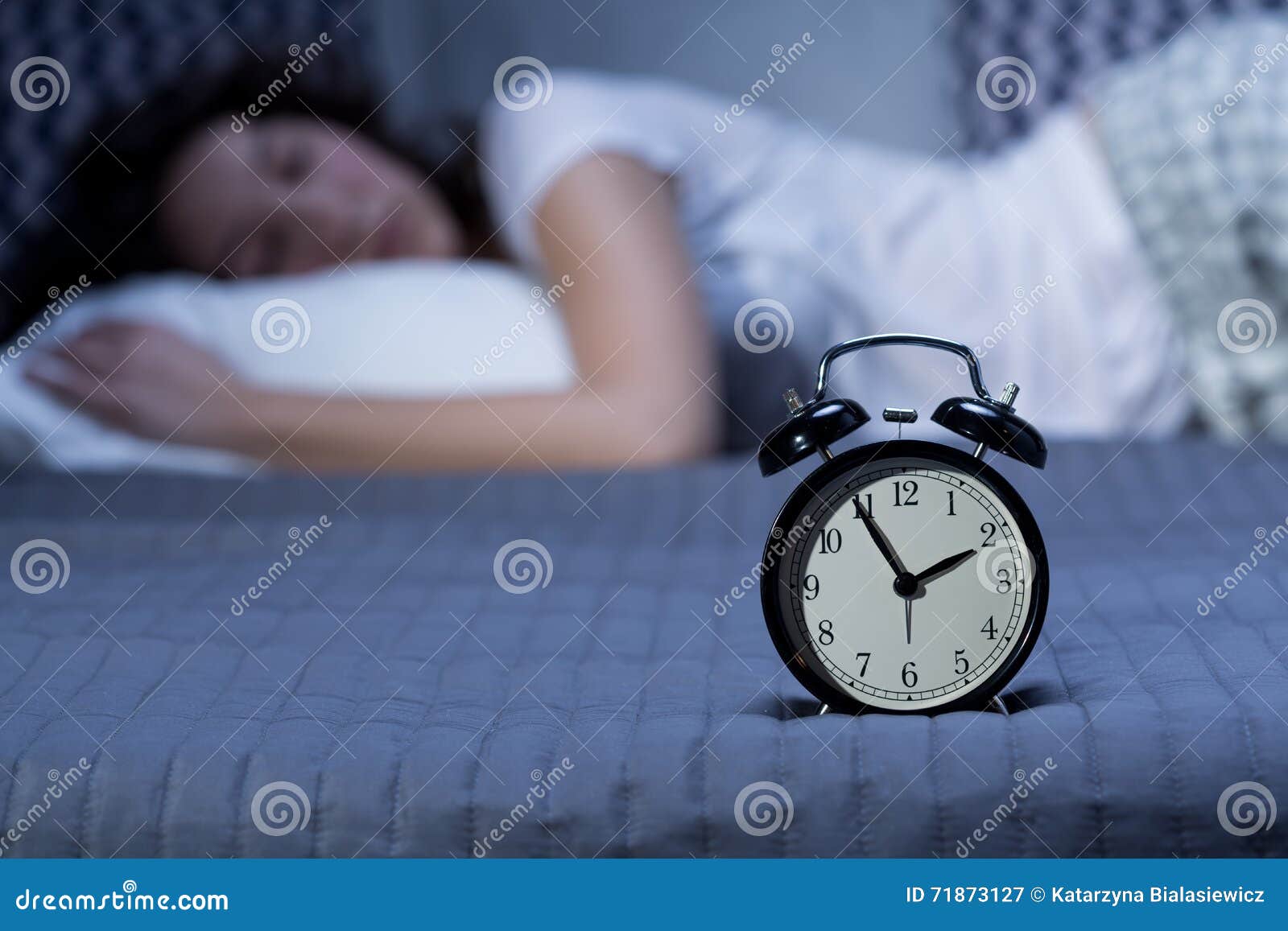 Finally asleep after a three-hour struggle. Close-up of a black, vintage alarm clock on a bed where a young woman is lying in the blurry background