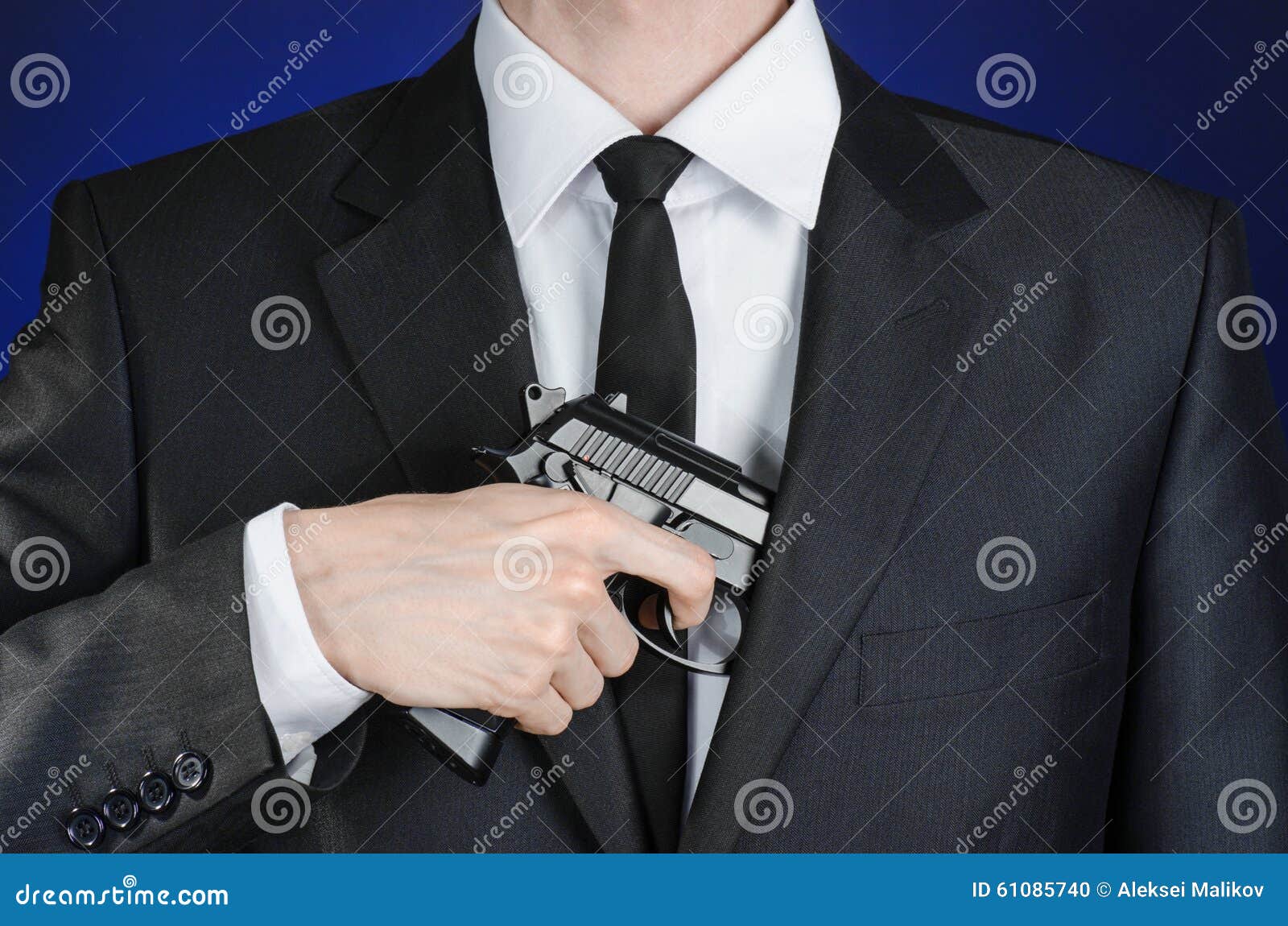 firearms and security topic: a man in a black suit holding a gun on a dark blue background in studio 