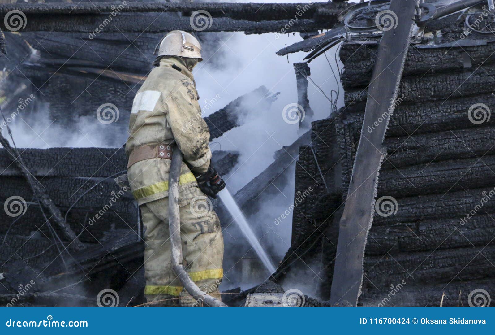 firefighter extinguishes the fire. fireman holding hose with water, watering strong stream of burning wooden structure in smoke.