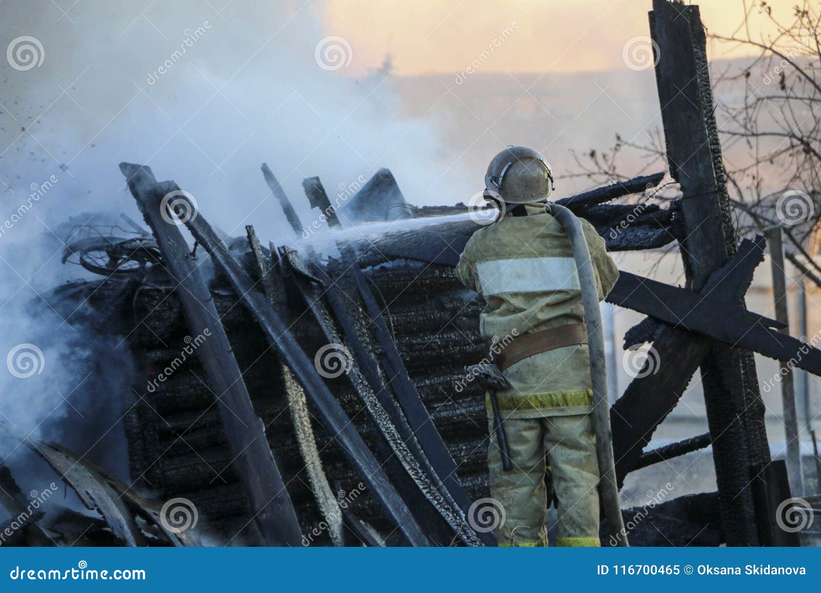 firefighter extinguishes the fire. fireman holding hose with water, watering strong stream of burning wooden structure in smoke.