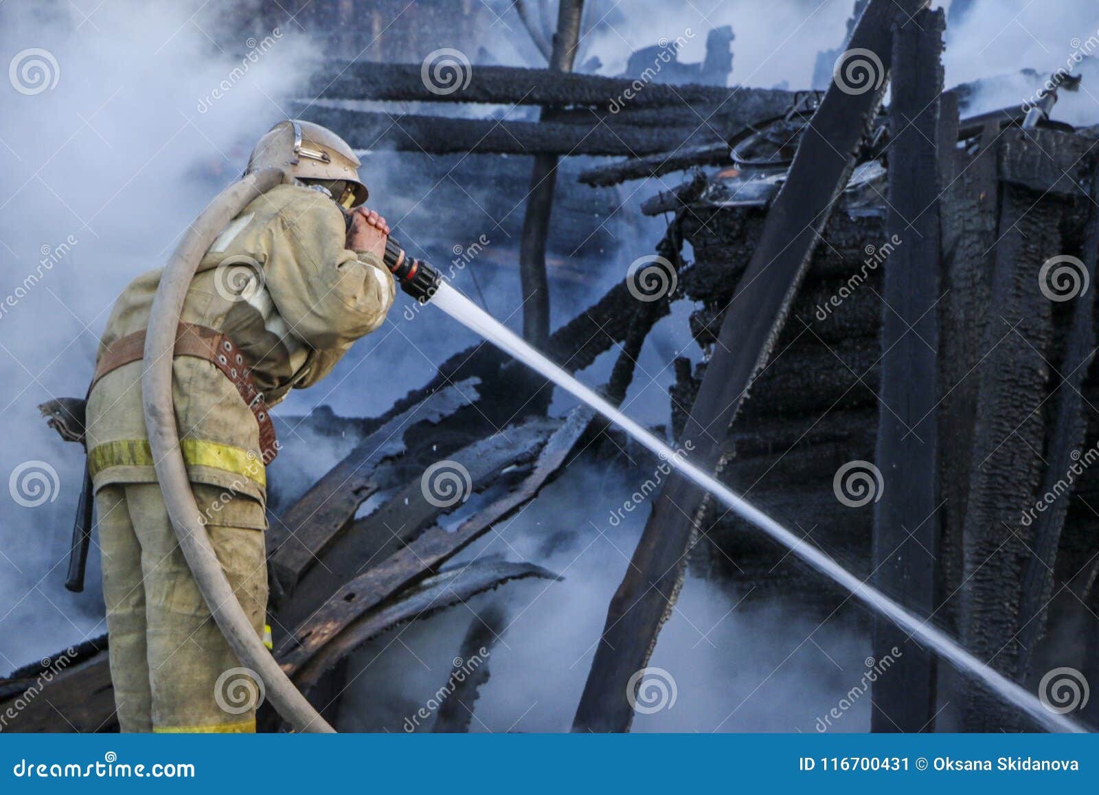 firefighter extinguishes the fire. fireman holding hose with water, watering strong stream of burning wooden structure in smoke.