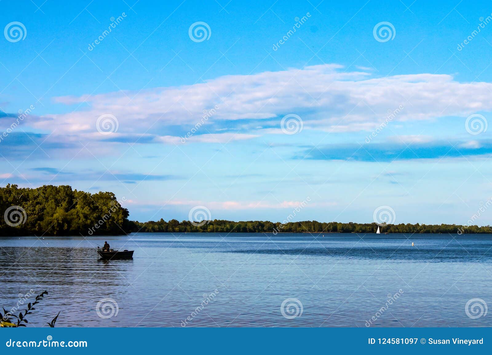fisherman in boat on lake with sailboat in the distance - lake erie