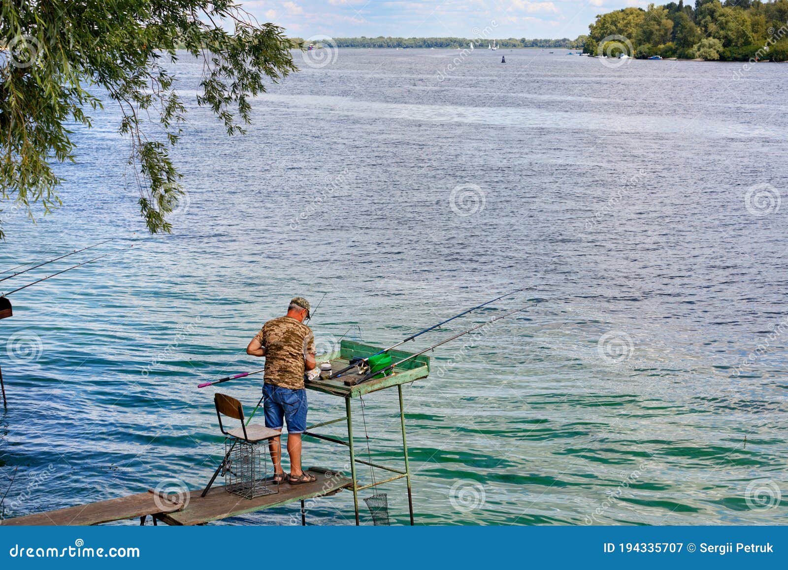 A Fisherman Catches Fish with Fishing Rods on the River Bank, Standing on a  Wooden Platform Stock Image - Image of green, equipment: 194335707