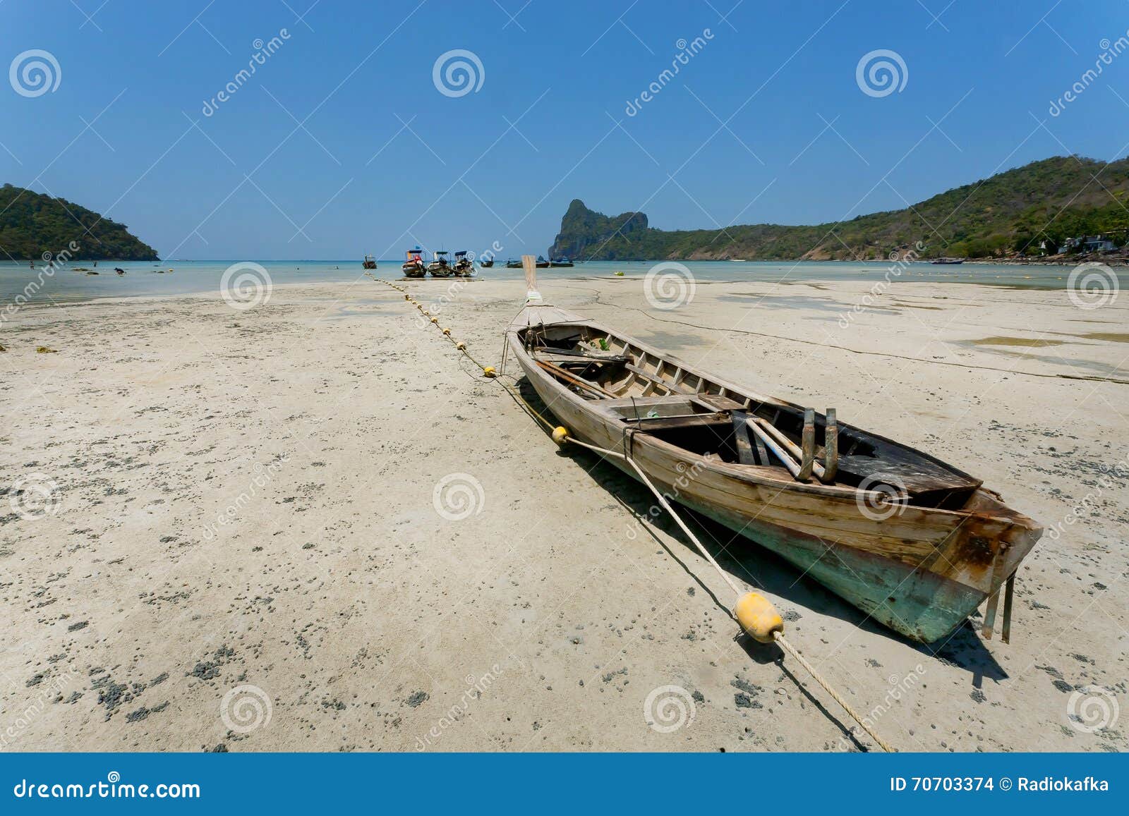 fishermen boat stranded in dry area of popular beach under blue sky.