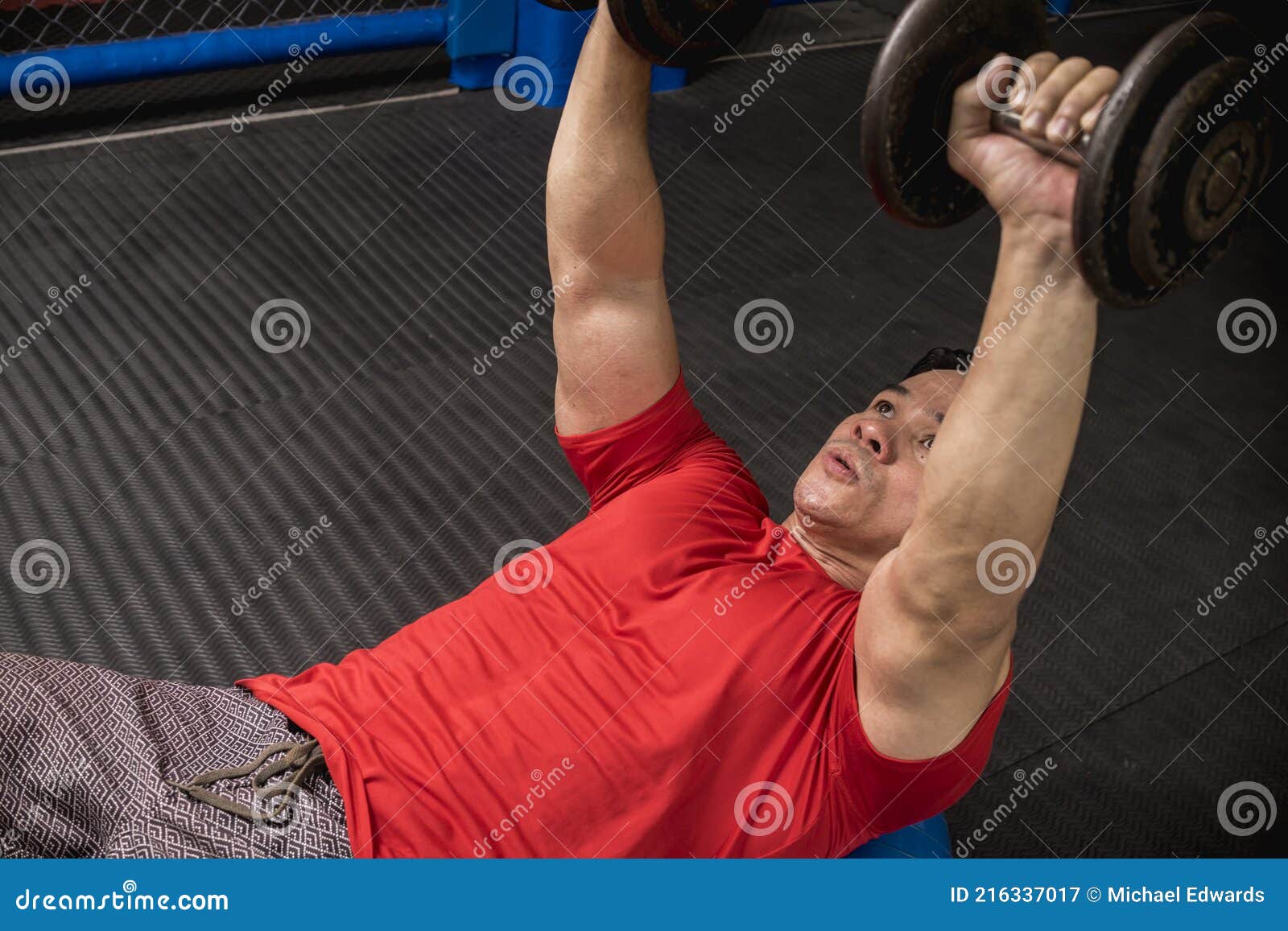 A Fit and Athletic Asian Guy Does Dumbbell Presses on a Stability Ball