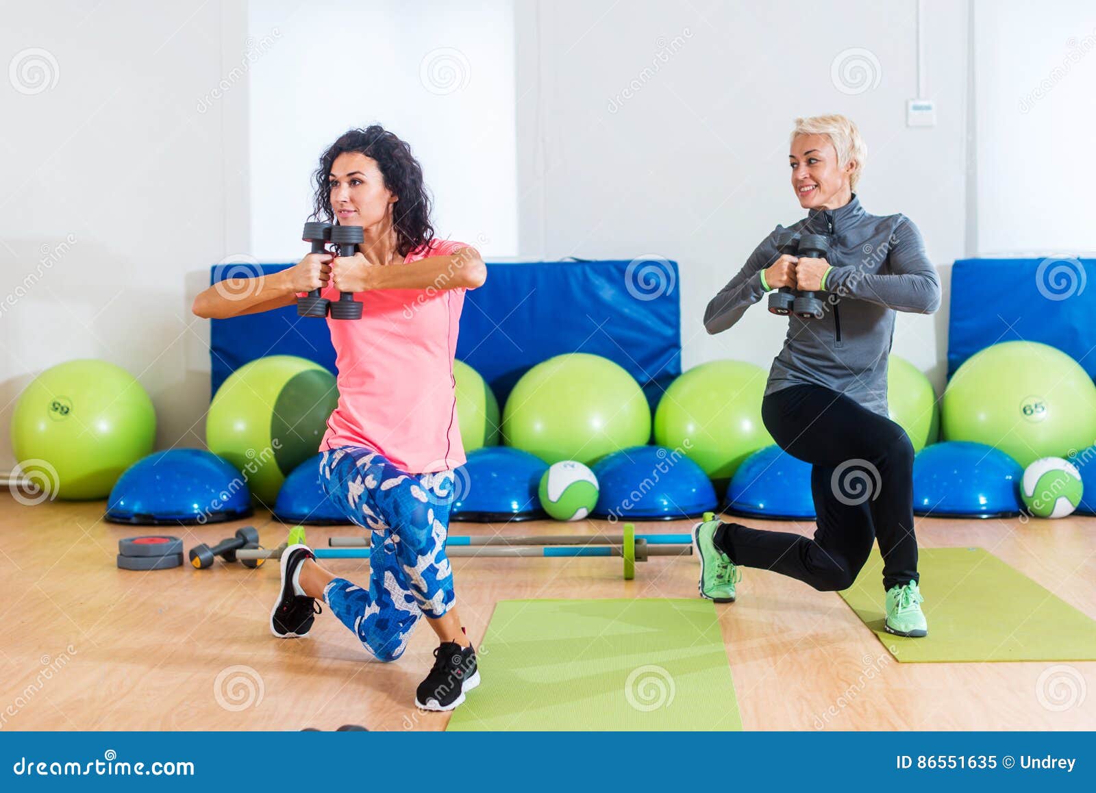 fit female sportswoman doing curtsy lunge exercise with dumbbells in group fitness studio class