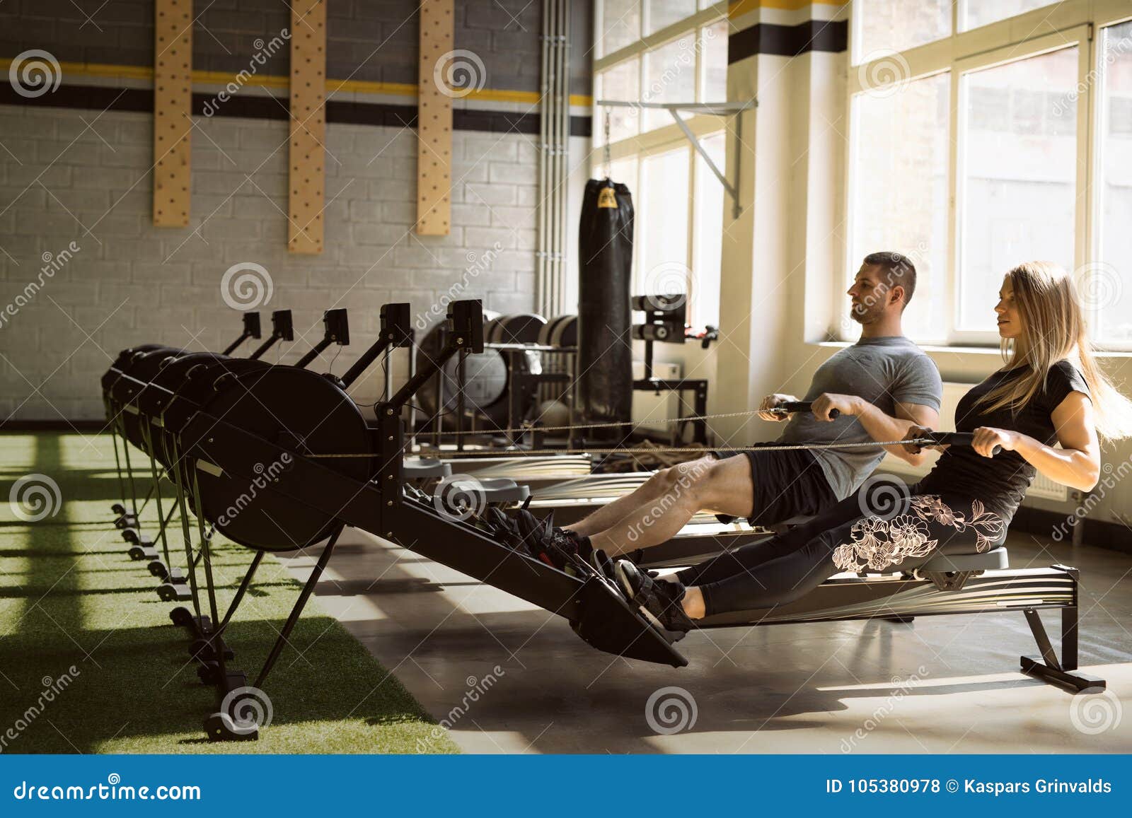 man and woman training on rowing machines in gym together