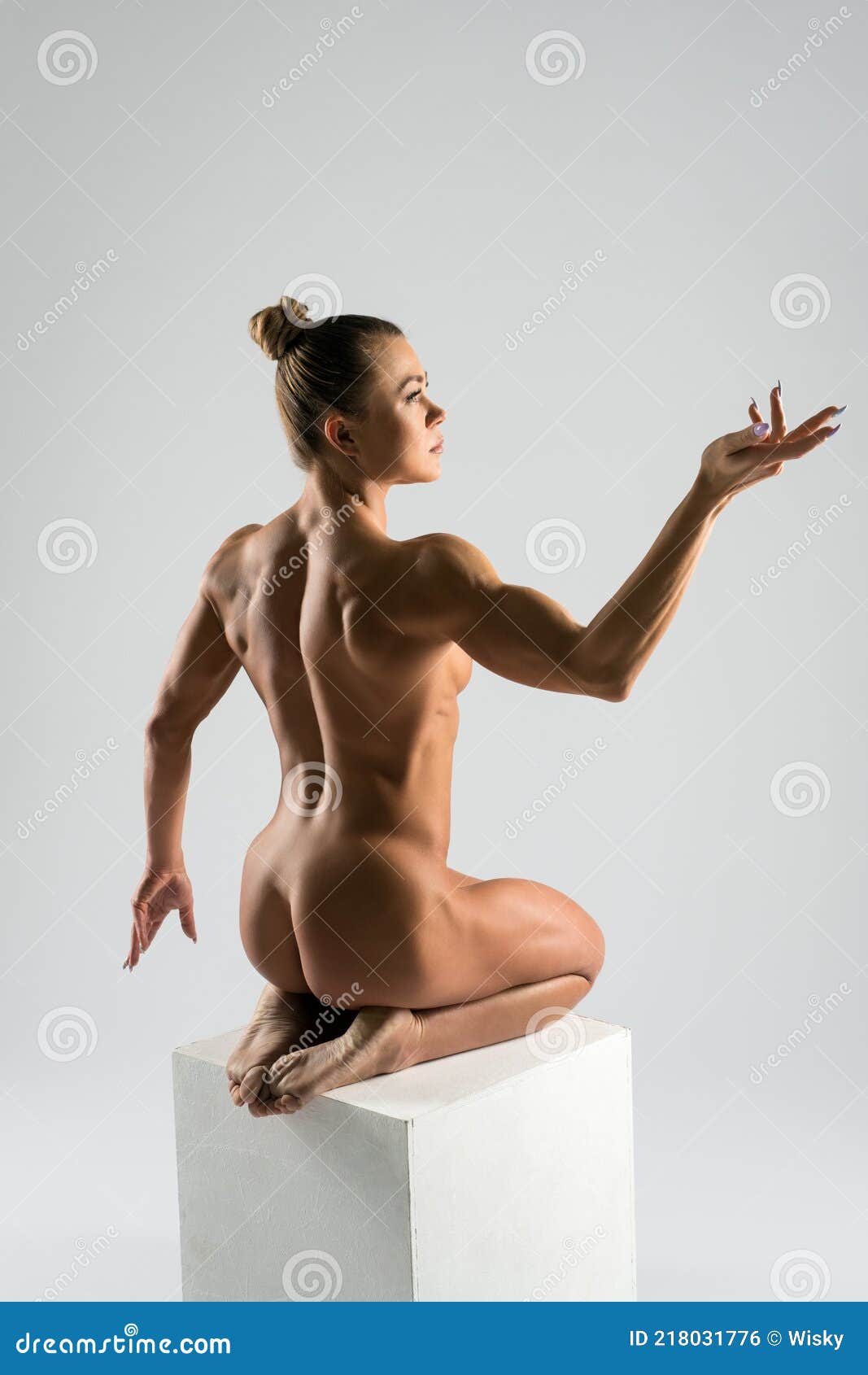 Fit Naked Woman Sitting on White Cube in Studio Stock Photo