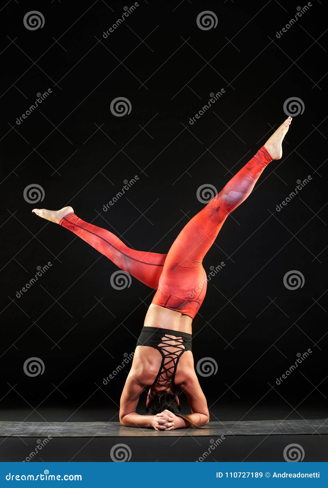 Fit toned woman doing a headstand with twist. Fit toned woman doing a headstand with legs open in a twist during a yoga workout full length over black with copy space