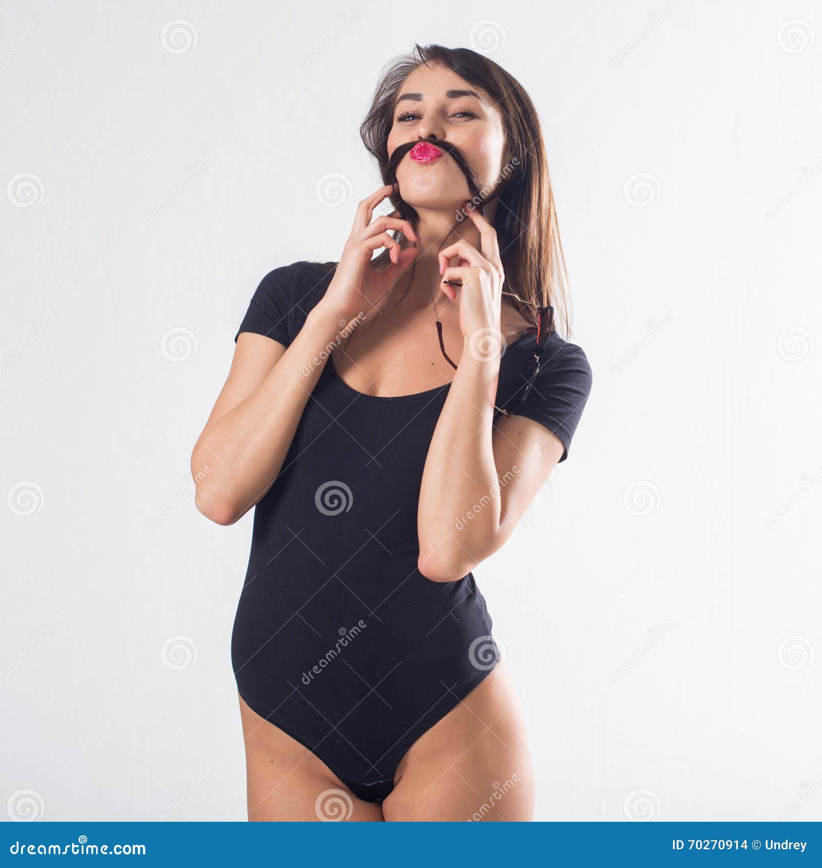 fit woman in black bodysuit holding hair strand, imitating, moustache, clowning, posing for a studio shot, not .