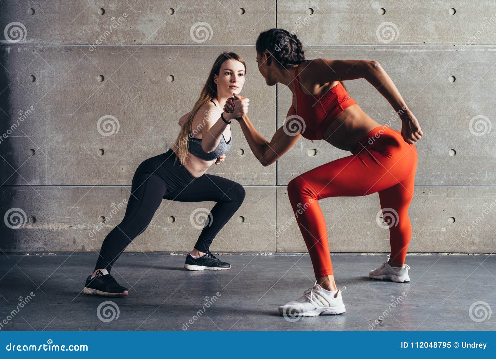 fit woman wrestle on hands with a female opponent looking in her eyes.