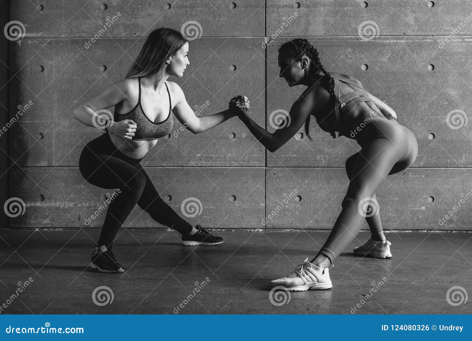 fit woman wrestle on hands with a female opponent looking in her eyes.