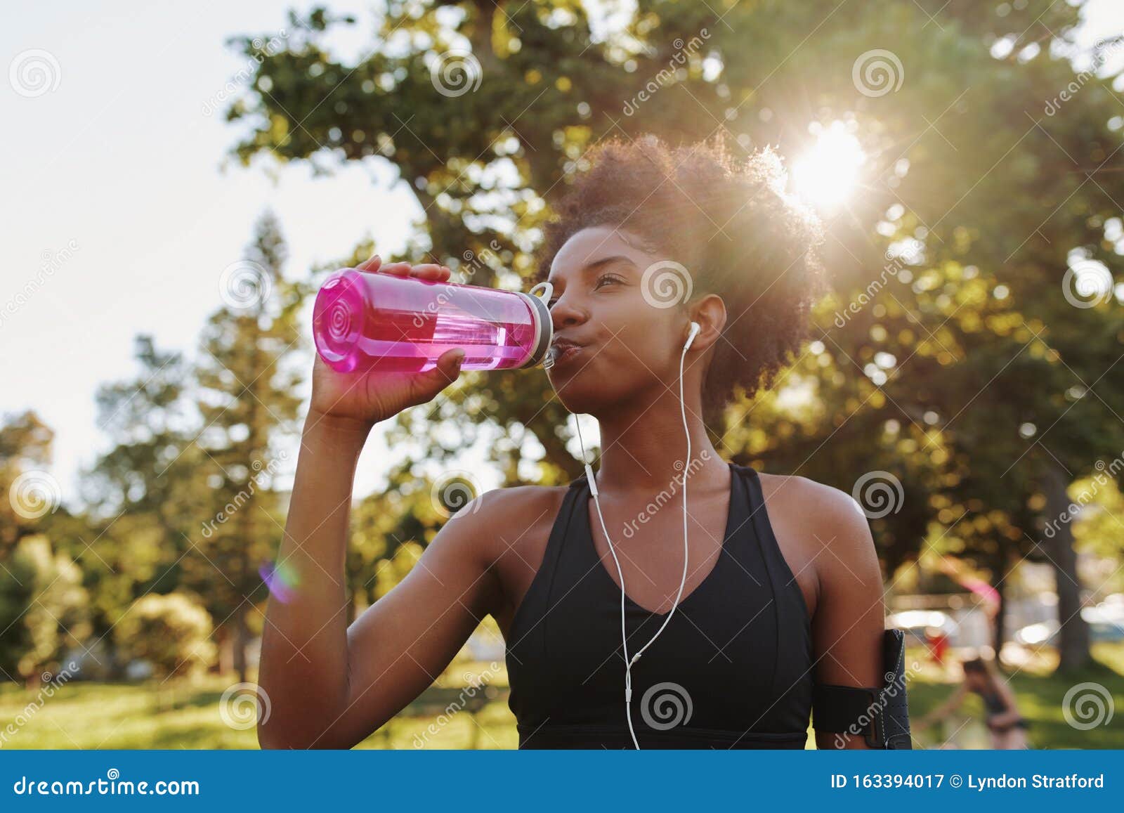 fitness athlete young african american woman listening to music on earphones drinking water in a reusable water bottle