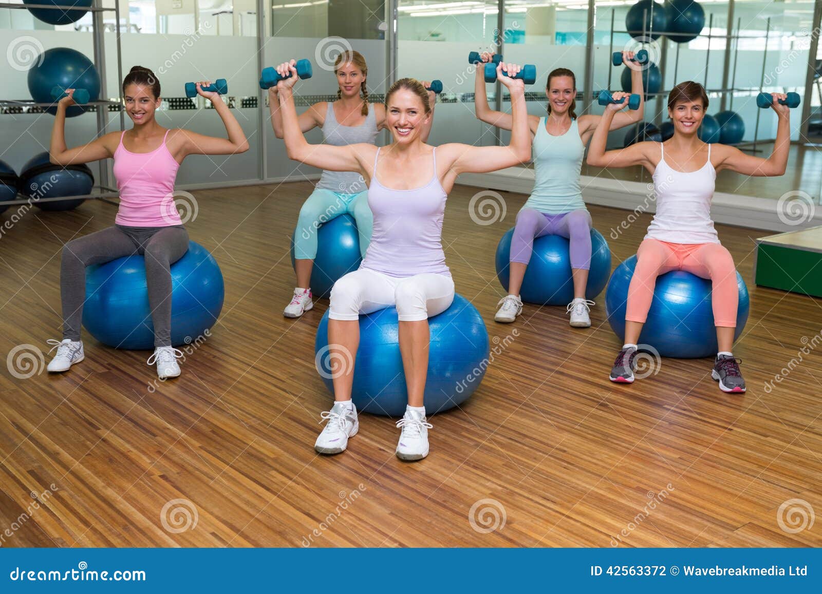 Fitness Class Holding Dumbbells on Exercise Balls in Studio Stock Photo