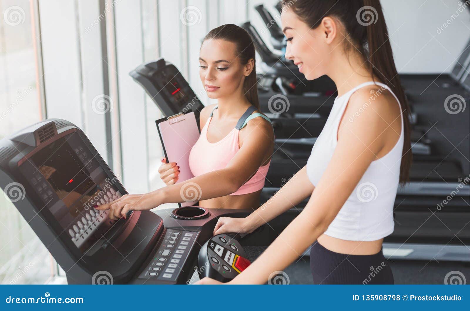 Fitness Instructor Helping Woman On Treadmill In Gym Stock Photo