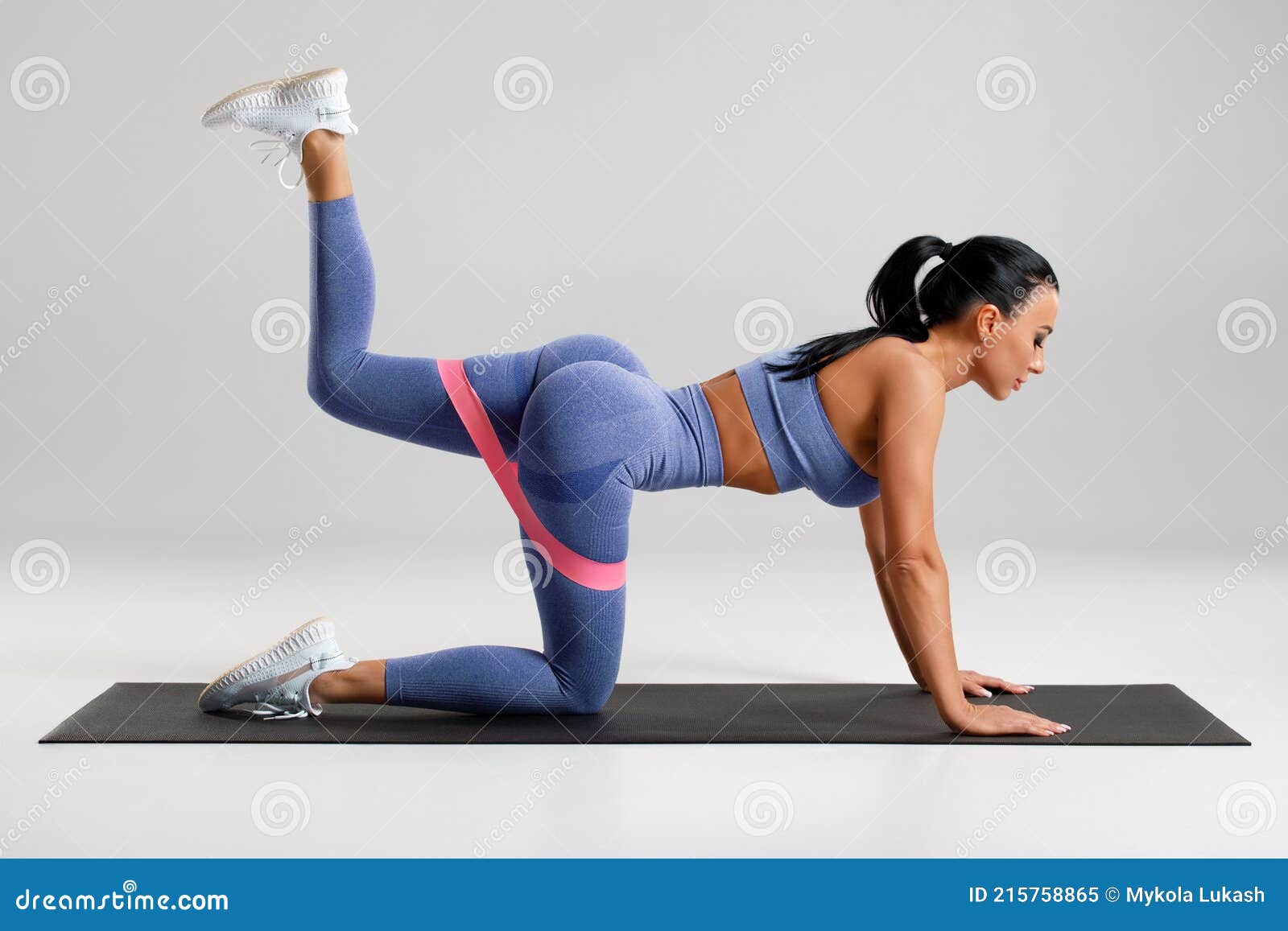 fitness woman doing kickback exercise for glutes with resistance band on gray background. athletic girl working out donkey kicks