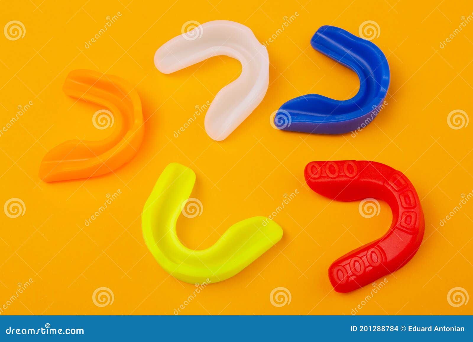 Five Boxing Mouthguards of Different Colors Lie on a Yellow Background