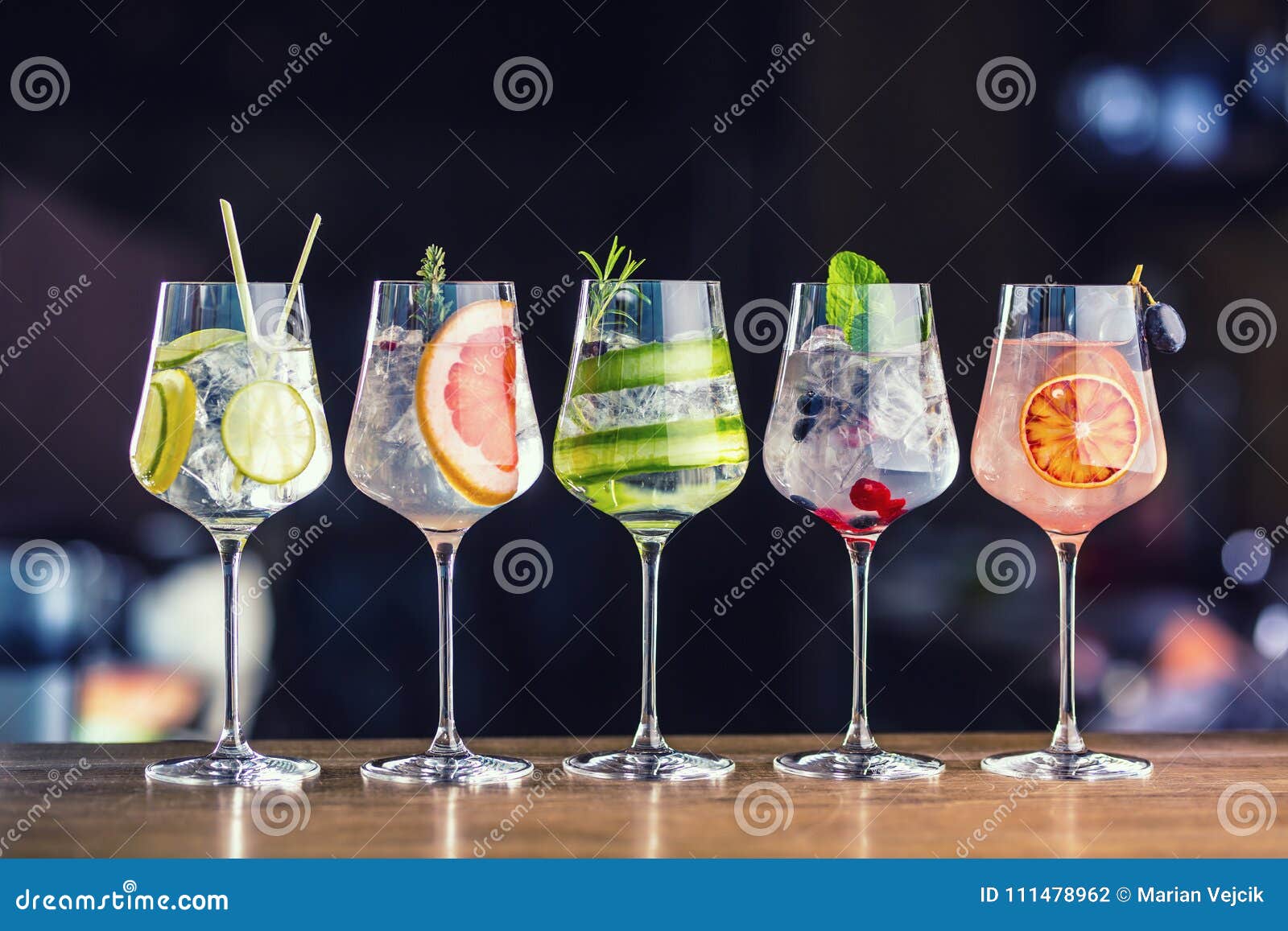 five colorful gin tonic cocktails in wine glasses on bar counter
