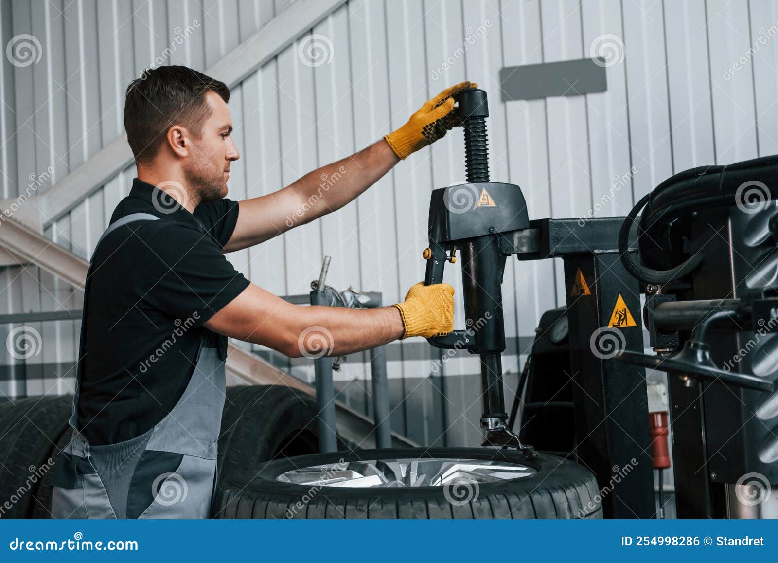 Fixing the Tire. Man in Uniform is Working in the Auto Service Stock