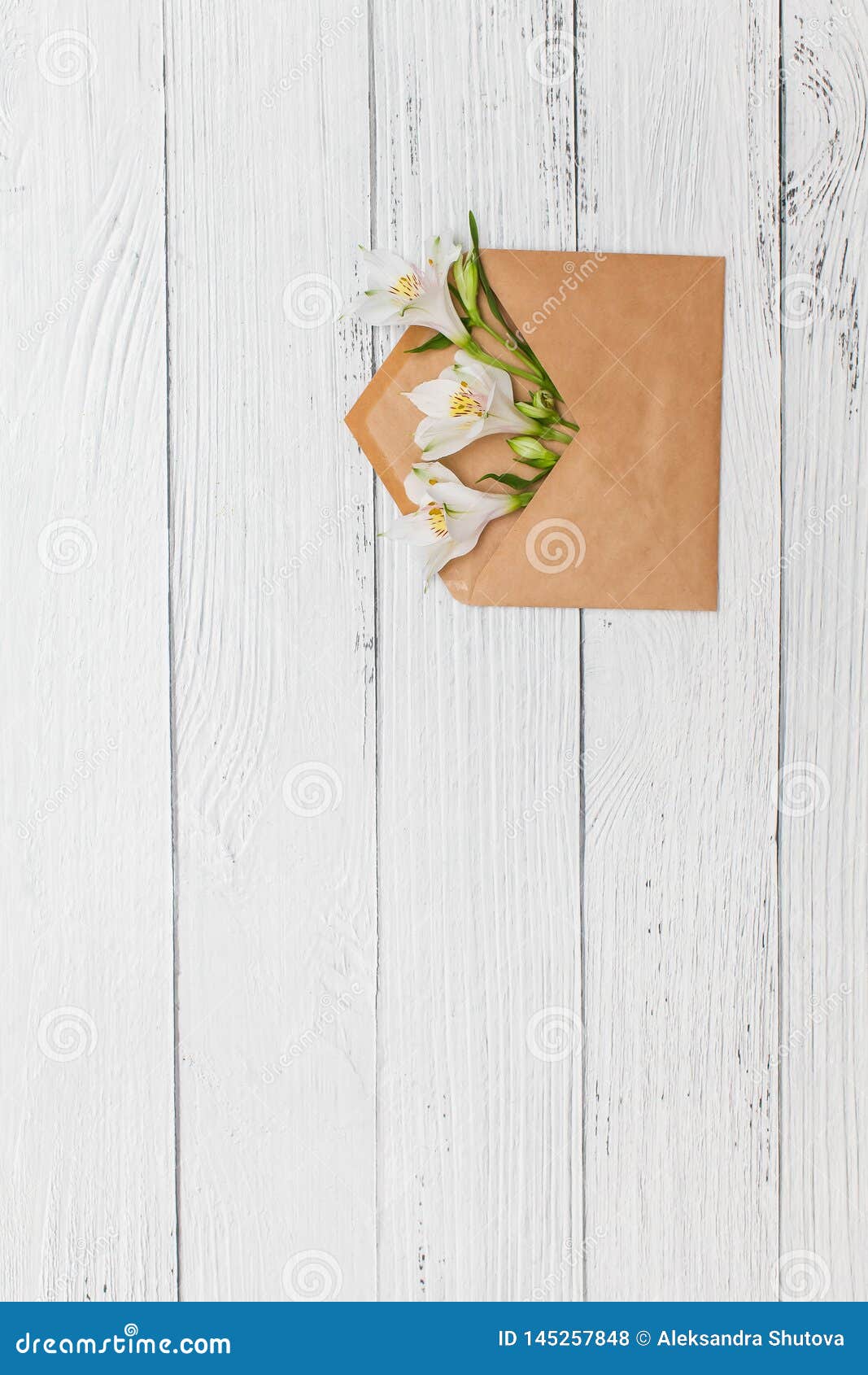 Flat lay with White lilies in craft envelope on old white wooden background