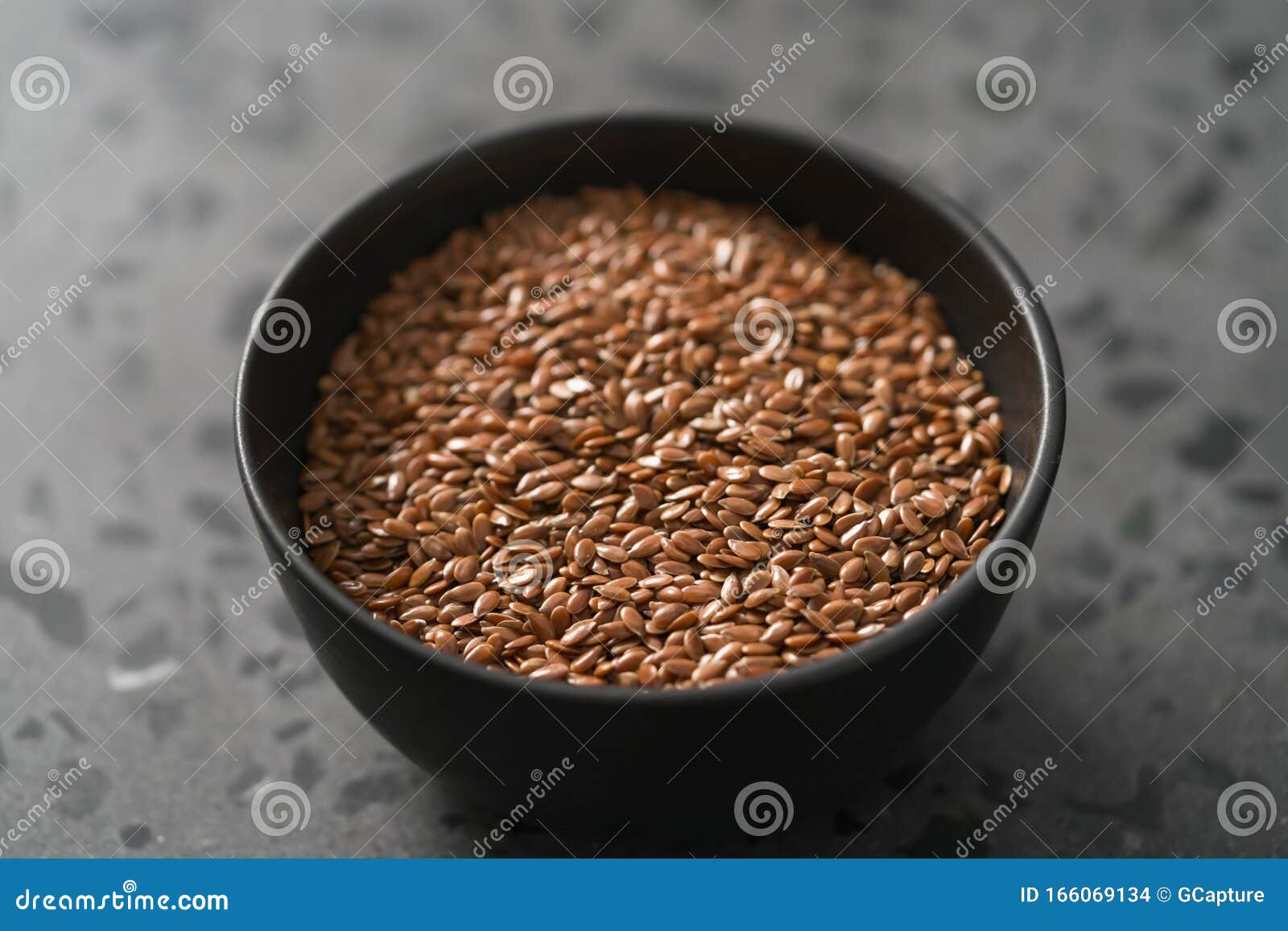 Flax Seeds in Black Bowl on Terrazzo Surface with Closeup Stock Photo