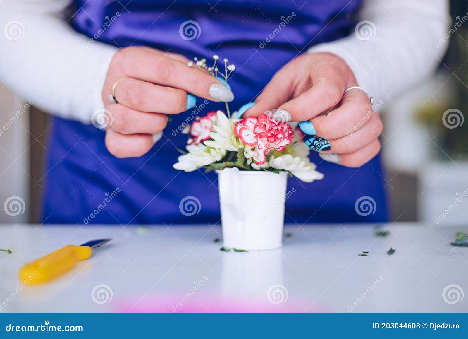 the florist hands creates a composition of flowers in a small white pot.