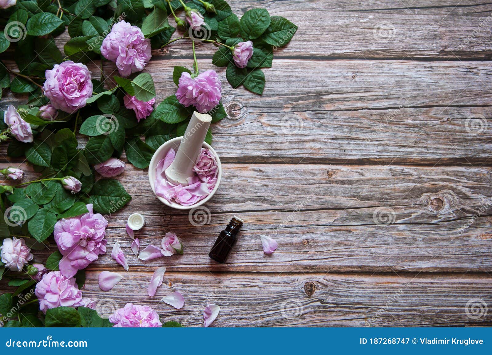 flowers and leaves of rosehip,  petals in a mortar with a pestle and a bottle of essential oil on a wooden background.