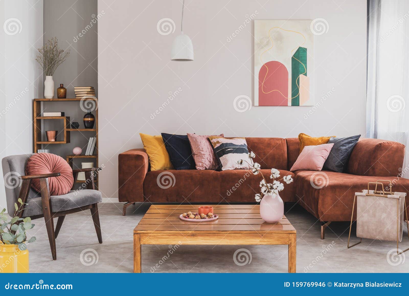flowers in vase on wooden coffee table in fashionable living room interior with brown corner sofa with pillows and abstract
