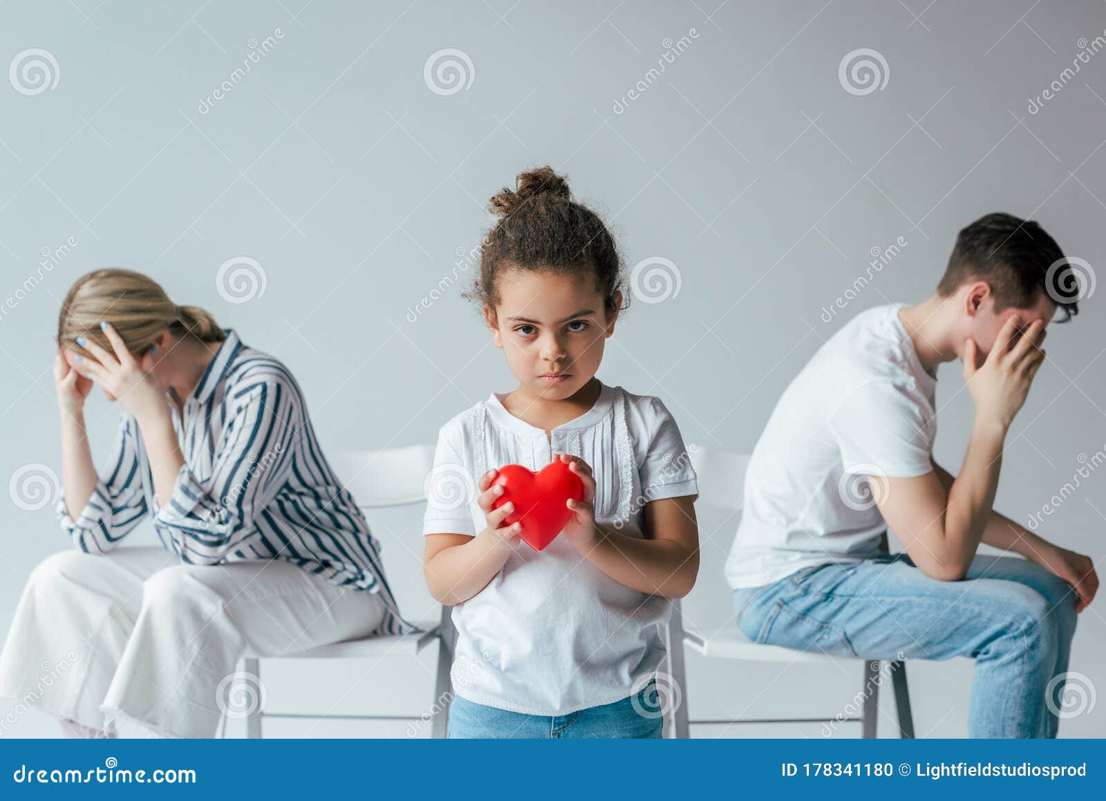 focus of adopted african american kid holding red heart near divorced foster parents on grey