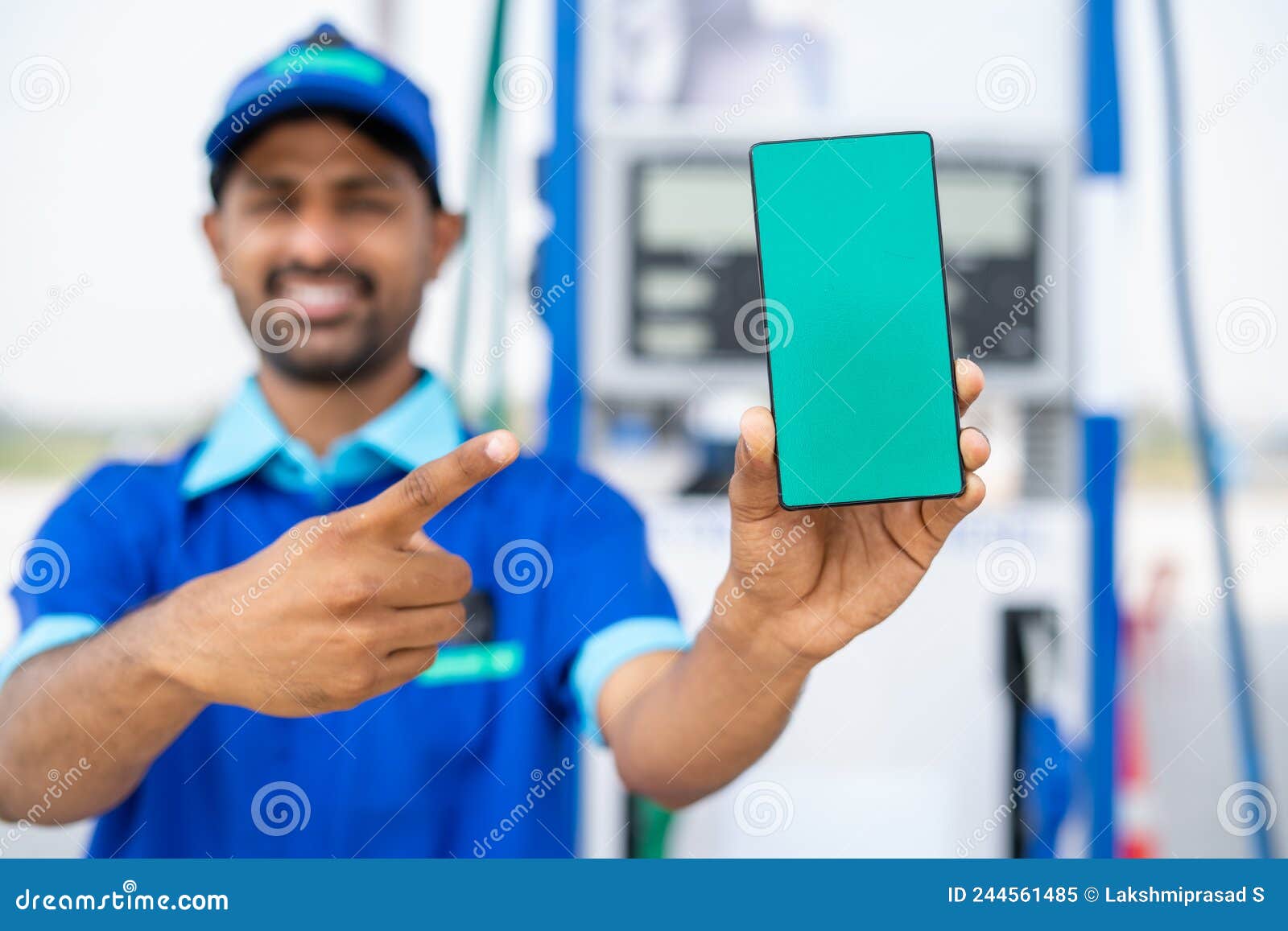 focus on phone, smiling petrol pump worker showing green screen mobile phone by pointing finger by looking at camera at