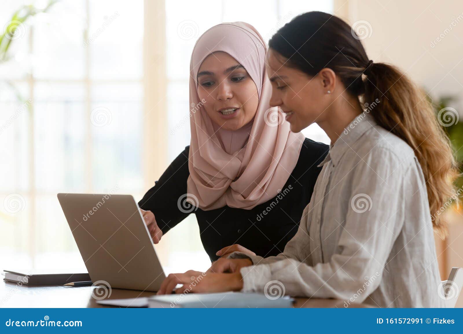 asian muslim female mentor teaching caucasian intern explaining computer work