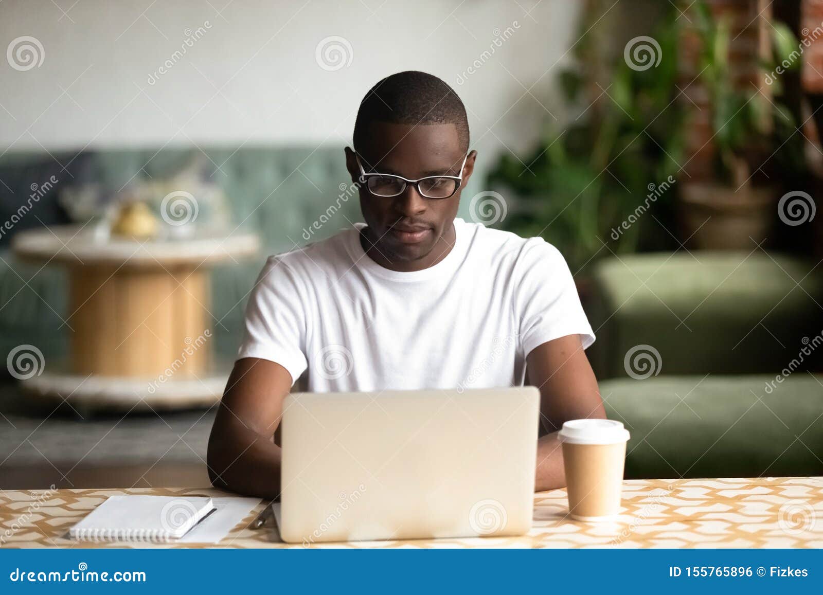 focused black man studying on laptop drinking coffee